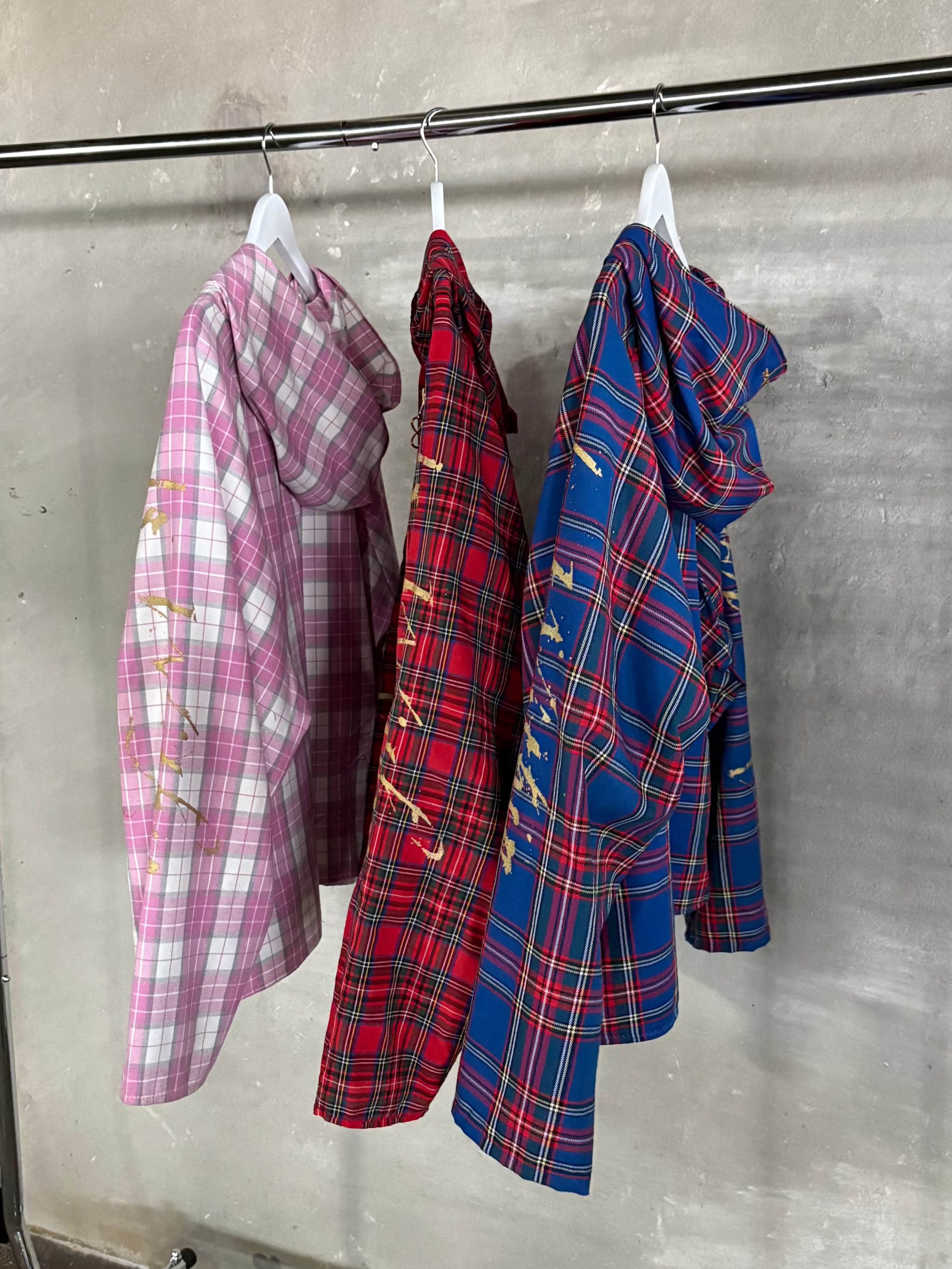 Three plaid shirts hanging on a rack against a gray wall.